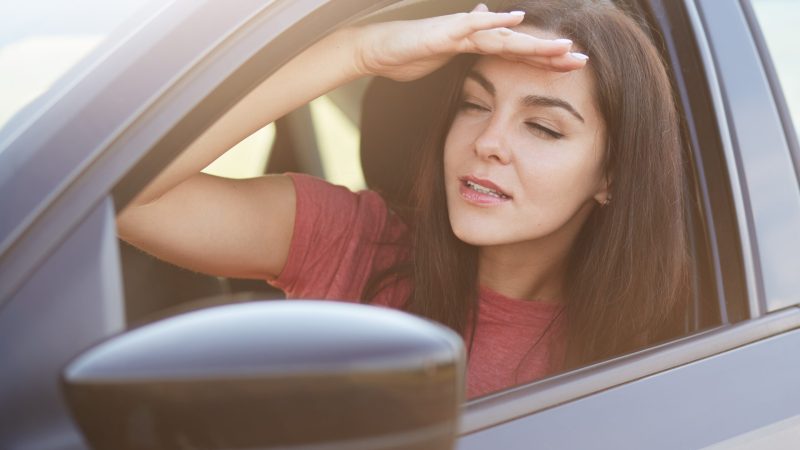 Attractive focused female keeps hand on forehead, looks into distance from car window, tries to notice something, has appealing appearance. Serious woman tries to see something through mist. Attractive focused female keeps hand on forehead, looks into distance from car window, tries to notice something, has appealing appearance. Serious woman tries to see something through mist.